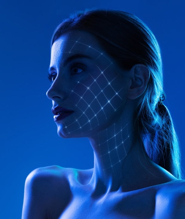 Trattamento viso Weyergans High Care a Milano Porta Romana Una donna di profilo sotto l'illuminazione blu, con una griglia luminosa proiettata sul viso e sul collo, su un solido sfondo blu.