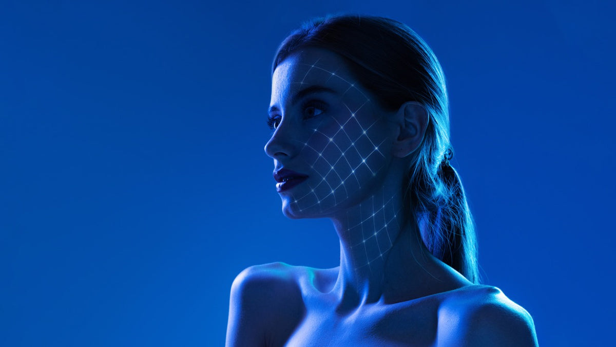 Trattamento viso Weyergans High Care a Milano Porta Romana Una donna di profilo sotto l'illuminazione blu, con una griglia luminosa proiettata sul viso e sul collo, su un solido sfondo blu.
